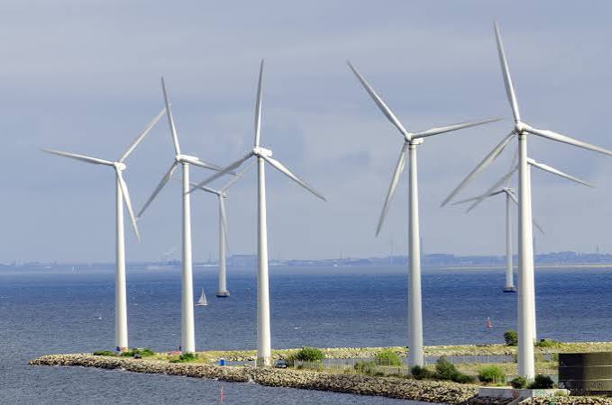 Offshore wind turbines along a rocky shoreline under a clear sky